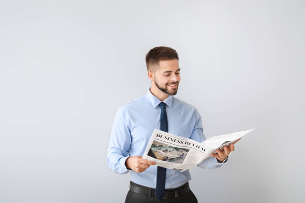 Handsome businessman with newspaper on light background - Photo, image