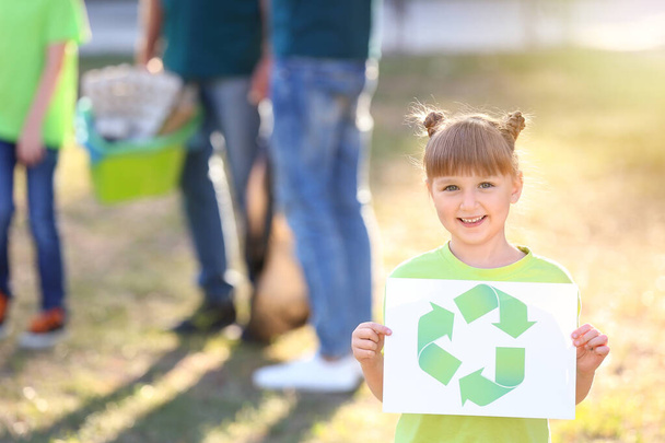 Mädchen hält Papierbogen mit Symbol für Recycling im Freien - Foto, Bild