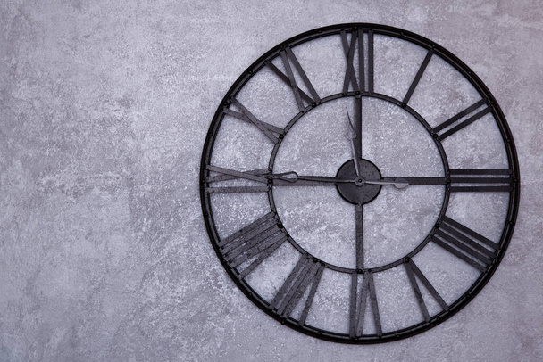 Orologio da parete vintage con numeri romani sul muro. parete grigia in stucco. L'orologio mostra un quarto a dodici 11: 45
 - Foto, immagini