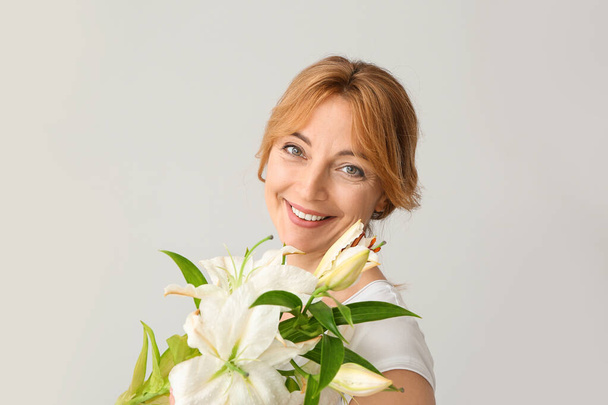 volwassen vrouw met mooie bloemen op lichte achtergrond - Foto, afbeelding