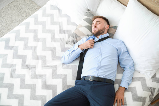 Κουρασμένος επιχειρηματίας με επίσημα ρούχα κοιμάται στο κρεβάτι - Φωτογραφία, εικόνα