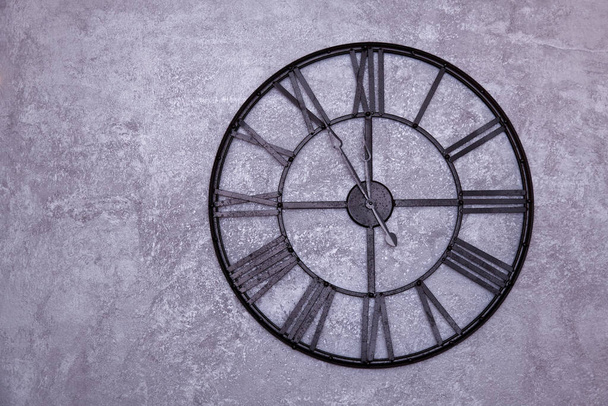Винтажные настенные часы с римскими цифрами на стене. серая штукатурка. Часы показывают от пяти до двенадцати 11: 55
 - Фото, изображение