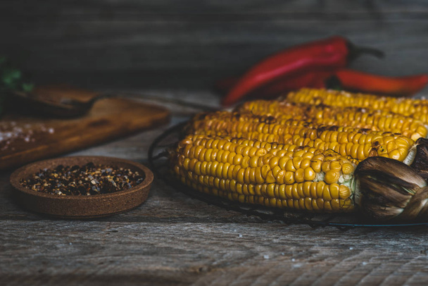 Grilled corn on the cob with herbs on a wooden board on a dark wooden background. - Фото, изображение