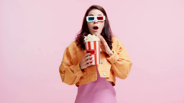 vystrašená dívka ve 3D brýle jíst popcorn izolované na růžové - Záběry, video
