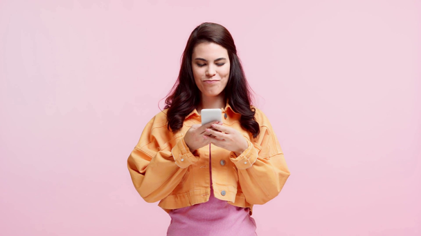 uśmiechnięta dziewczyna smsy na smartfonie odizolowany na różowy - Materiał filmowy, wideo
