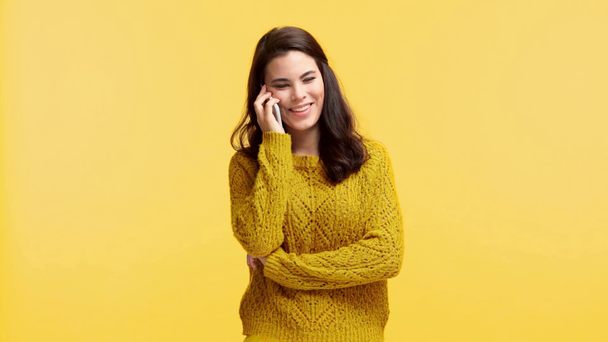 lachend meisje in trui praten op smartphone geïsoleerd op geel - Video