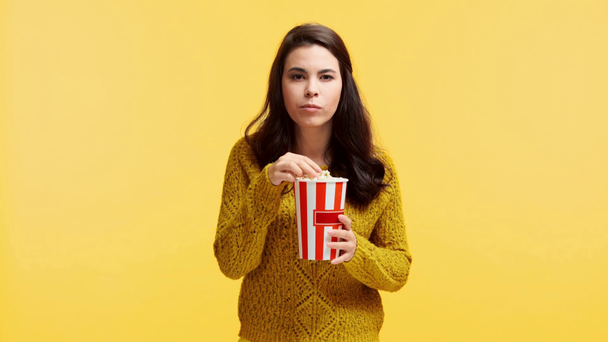 geconcentreerd meisje in trui eten popcorn geïsoleerd op geel - Video