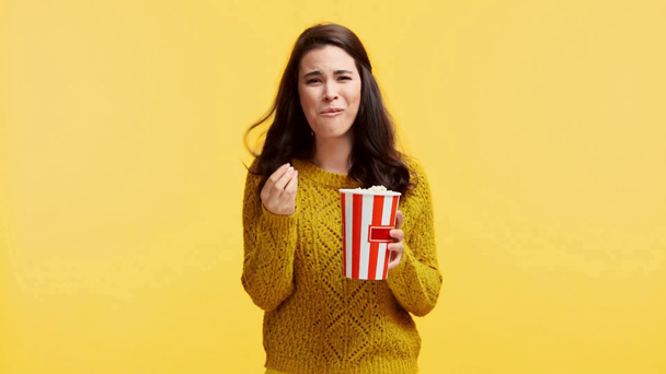 smějící se dívka ve svetru jíst popcorn izolované na žluté - Záběry, video