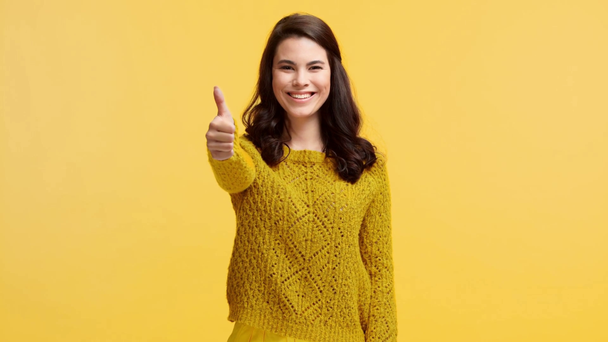 smiling girl in sweater showing thumb up isolated on yellow - Footage, Video