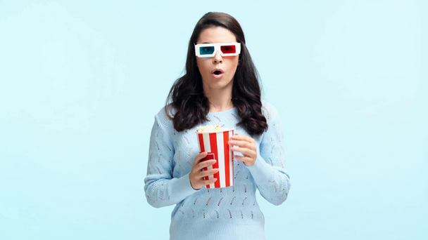 šokované dívka v 3D brýle jíst popcorn izolované na modré - Záběry, video