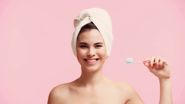 χαμογελαστό γυμνό κορίτσι με πετσέτα στο κεφάλι κρατώντας οδοντόβουρτσα απομονωμένη σε ροζ - Πλάνα, βίντεο