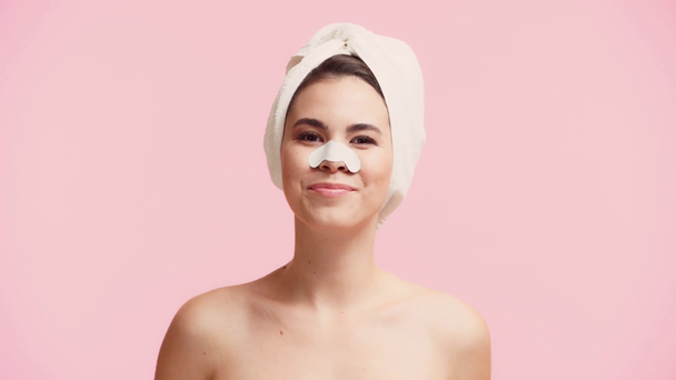 smiling naked girl with towel on head applying patch on nose isolated on pink - Video