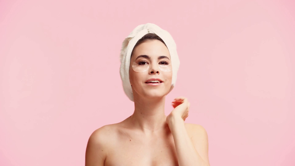 χαμογελαστό γυμνό κορίτσι με πετσέτα στο κεφάλι και τα μάτια μπαλώματα μασάζ πρόσωπο απομονώνονται σε ροζ - Πλάνα, βίντεο