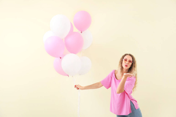Belle jeune femme avec des ballons souffle baiser sur fond de couleur - Photo, image
