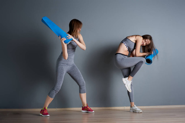 Sporty women fighting twisted blue rugs against gray empty wall - Photo, Image