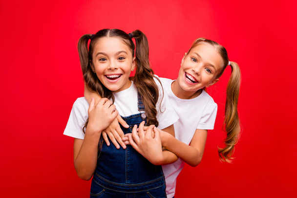 Photo of two funny pretty small ladies spending weekend time together buddies enjoy best holidays wear jeans overall white t-shirt isolated red color background - Photo, Image