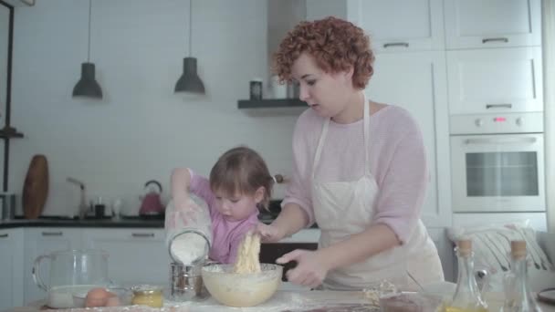 Anya a lányával a konyhában egy tányéron gyúrja a tésztát. Egy lány csintalan a konyhában. Anya főz a kislányával. Az anya megtanítja a gyerekét főzni. Vidám főzés sütés. - Felvétel, videó