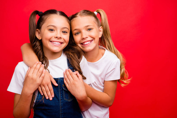Photo of two funny pretty small ladies hugging spending weekend time together enjoy best holidays wear jeans overall white t-shirt isolated red color background - Φωτογραφία, εικόνα
