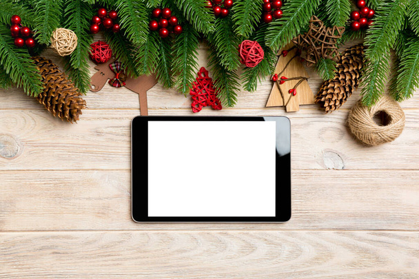 Top view of tablet, Christmas toys, decorations and fir tree branches on wooden background. New Year holiday concept with copy space - Photo, Image