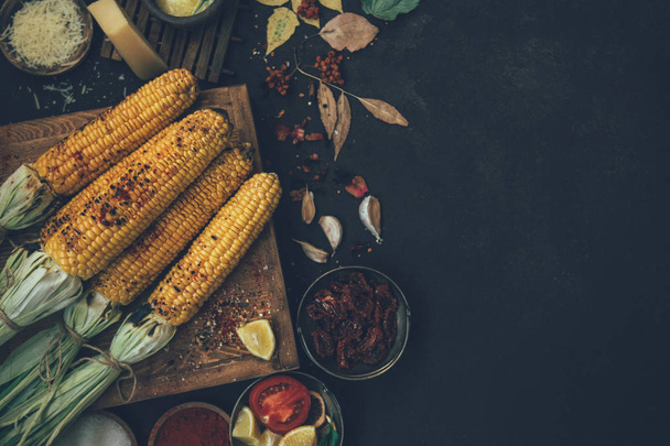 Corn grilled with cheese and spices on the dark rustic background. Autumn food background. Fast food in the summer or fall. Toned image. Flat lay with copy space. - Photo, image