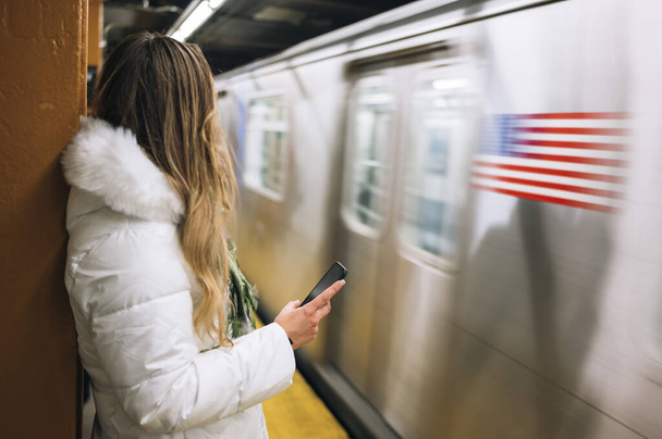 Donna in piedi vicino alla metropolitana di passaggio con smartphone
 - Foto, immagini