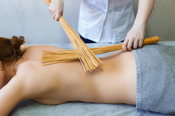 Back massage in the massage room with bamboo brooms. Massage therapist massaging woman back with a bamboo. - Фото, изображение