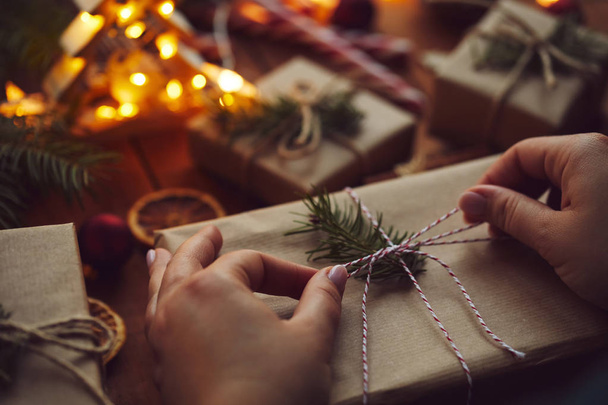 Woman wrapping Christmas present on table full of decorations - Фото, изображение