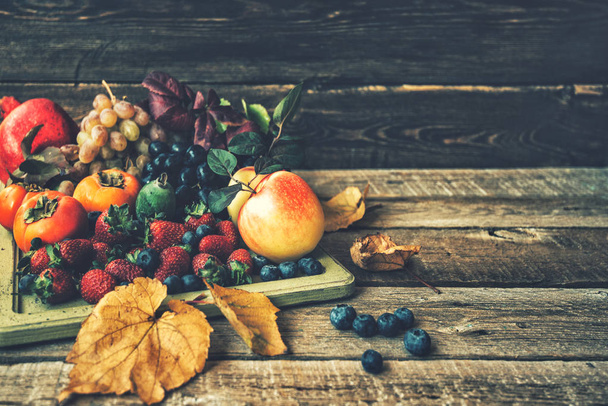 Assorted fresh ripe fruits and vegetables. Food concept background. Autnum harvest. Strawberries, blueberries apples, grapes, persimmon, pomegranate and fall leaves. Toned vintage with copy space. - Foto, Imagen
