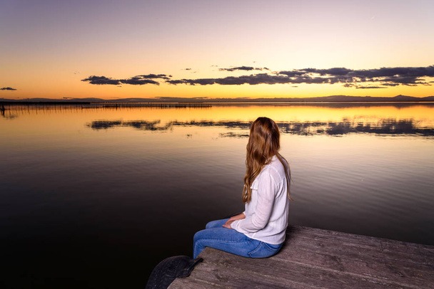 langharige jonge vrouw ontspannen bewonderend de gouden zonsondergang op een - Foto, afbeelding
