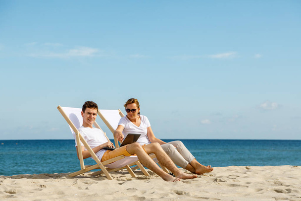 Woman and man basking in the sun sitting in loungers using laptop - Foto, Bild