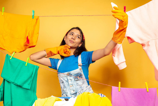 Funny and beautiful housewife doing housework on yellow background - Φωτογραφία, εικόνα