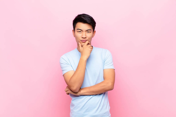 young chinese man looking serious, confused, uncertain and thoughtful, doubting among options or choices against flat color wall - Fotoğraf, Görsel