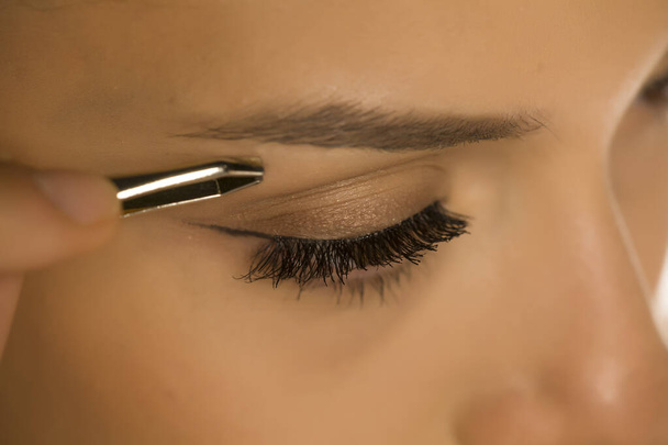 Nahaufnahme einer Frau, die sich mit einer Pinzette die Augenbrauen zupft - Foto, Bild