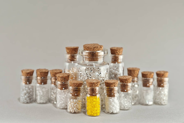 White, beige and yellow beads in glass jars on a gray background. Beads in a transparent container with a wooden cork. - Foto, Imagen