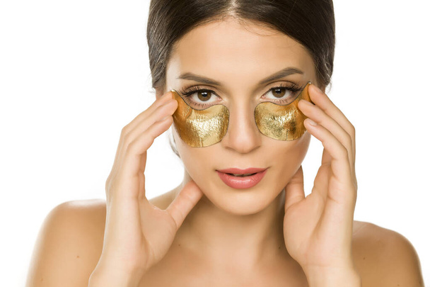 Young beautiful woman posing with golden patches under her eyes on white background - Foto, Imagen