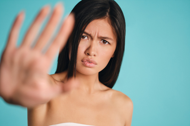 Upset Asian brunette girl showing stop gesture sadly looking in camera over colorful background - Photo, Image