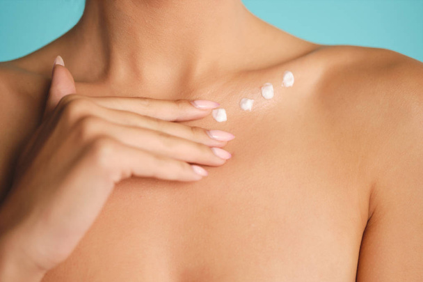 Close up young woman body with points of cream on clavicle over colorful background - Foto, afbeelding