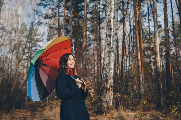 woman funs with a colorful umbrella walks in the woods. autumn park. The concept of fashion, accessories, outdoor walks - Foto, Bild
