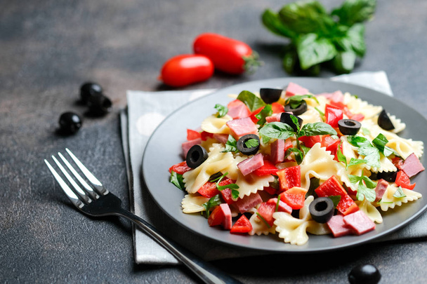 Traditional salad with pasta farfalle, ham, pepper and herbs on a dark plate on a dark background copy space - Photo, Image