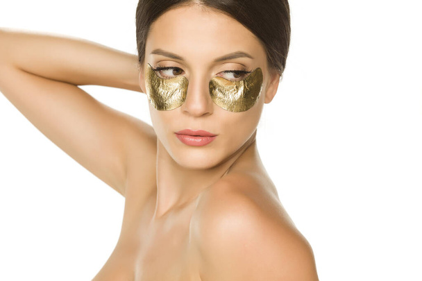 Jovem bela mulher posando com manchas douradas sob seus olhos no fundo branco
 - Foto, Imagem