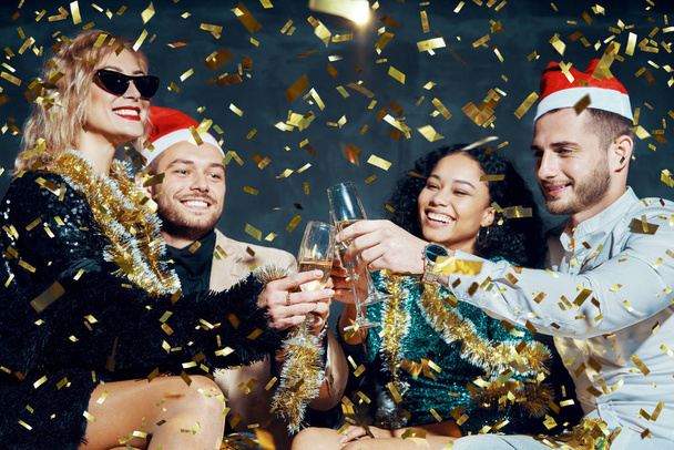 Többnemzetiségű boldog barátok pohárköszöntőt pezsgővel ünneplik a karácsonyt vagy az újévet, gratulálnak egymásnak és élvezik a partit - Fotó, kép
