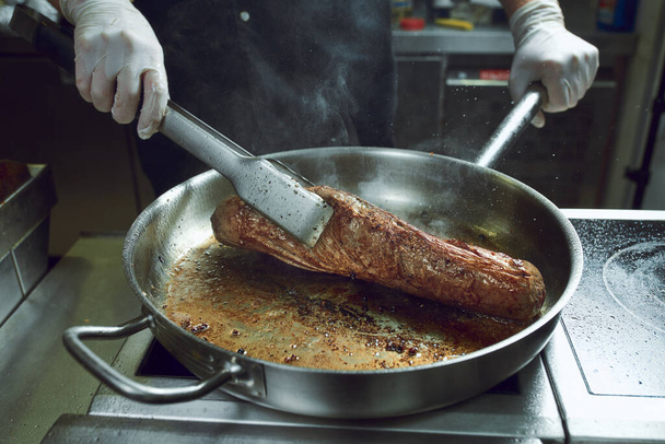 The chef works in the kitchen of the restaurant. Fresh meat roasted in a large frying pan. Restaurant kitchen background - Photo, Image