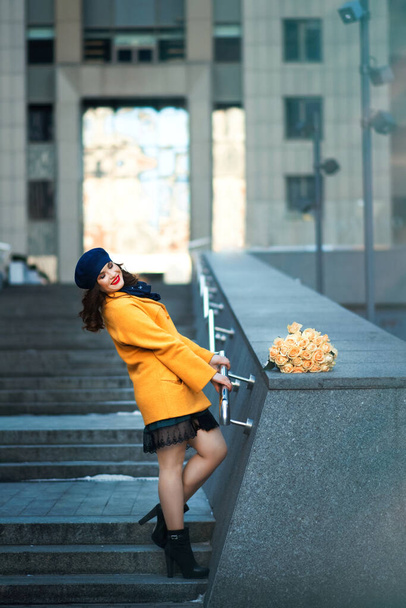 Stylish woman with roses and red lipstick in bright yellow coat and blue hat - 写真・画像