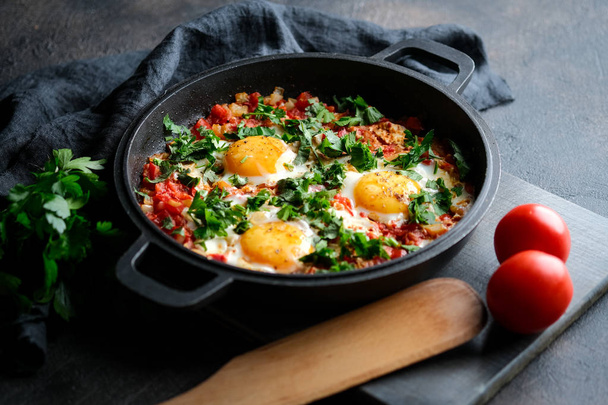 Geleneksel Shakshuka, yumurta, domates ve maydanozlu, siyah arka planda demir bir tavada.  - Fotoğraf, Görsel