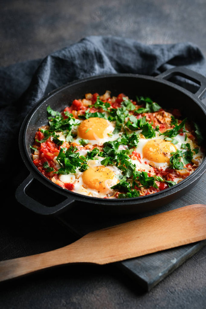 Traditional  shakshuka with eggs, tomato, and parsley in a iron pan on a dark background  - Fotoğraf, Görsel