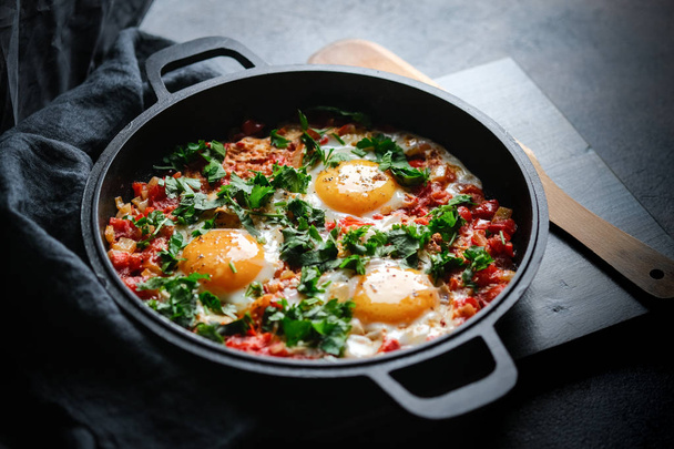 Традиційна шшука з яйцями, помідорами та петрушкою на залізній сковороді на темному тлі
  - Фото, зображення