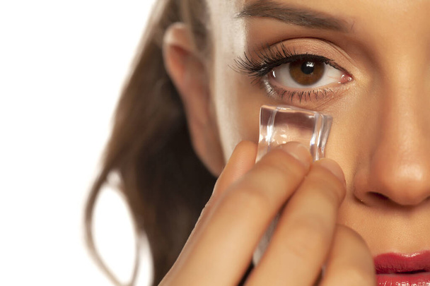 young beautiful woman holding ice cube under the eye on white ba - Photo, Image