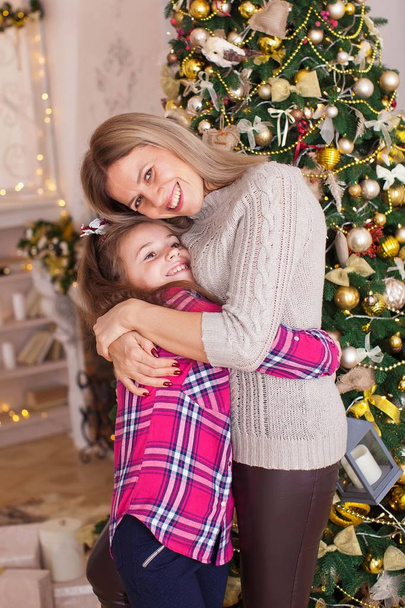 ママと娘はクリスマスツリーの近くで面白い本を抱いて笑ってる - 写真・画像