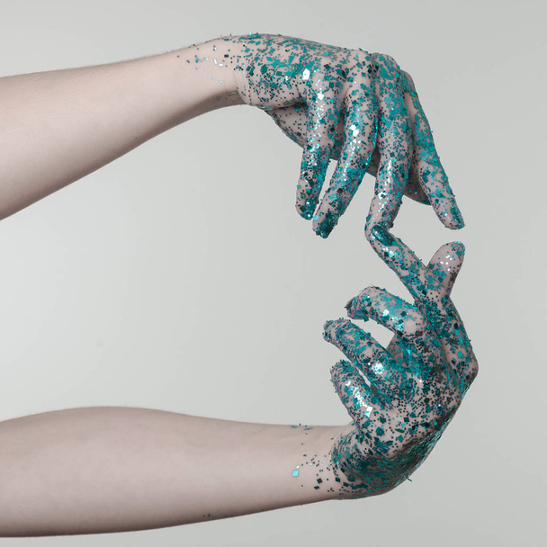 Beautiful woman hands with blue glitter in front of black, can be used as background - Foto, afbeelding