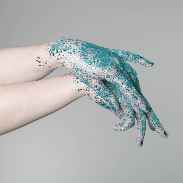 Beautiful woman hands with blue glitter in front of black, can be used as background - Photo, image